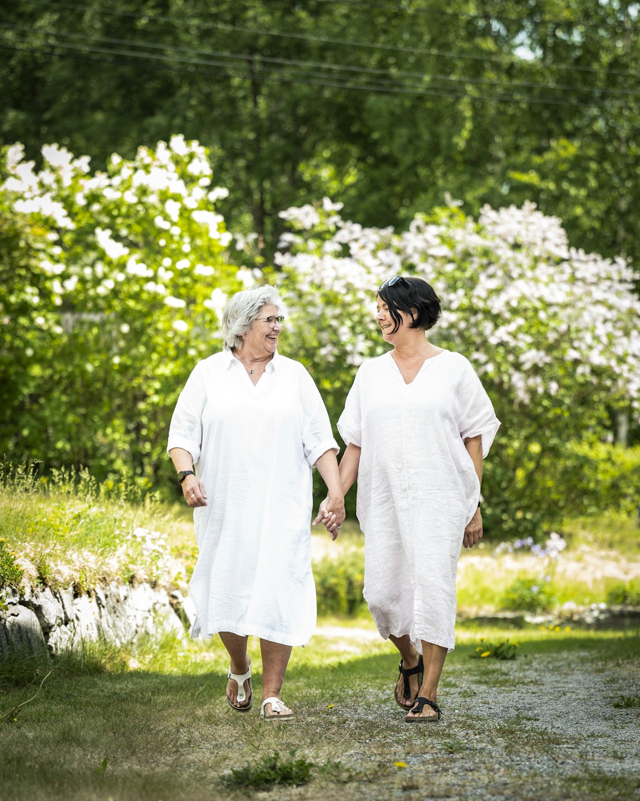To kvinner kledd i hvitt vandrer i det grønne mens de holder hender