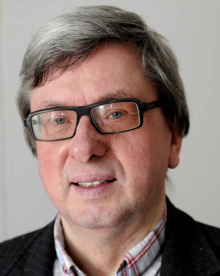 Portrettfoto av en lys mann med grått hår og firkantede svarte briller.